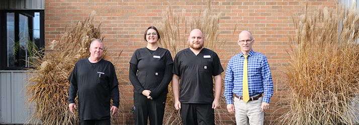 Chiropractor Lansing MI Charles Roost And Daniel Dail With Team In Front Of Brick Wall